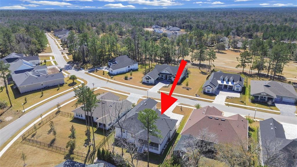 An aerial view shows a suburban neighborhood with houses, streets, and surrounding wooded areas — 4716 HICKORY OAK DRIVE, BROOKSVILLE, FL