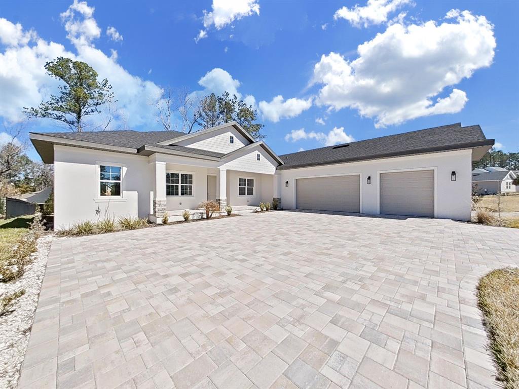 A single-story house with a white exterior, stone accents, and a large paved driveway — 4716 HICKORY OAK DRIVE, BROOKSVILLE, FL