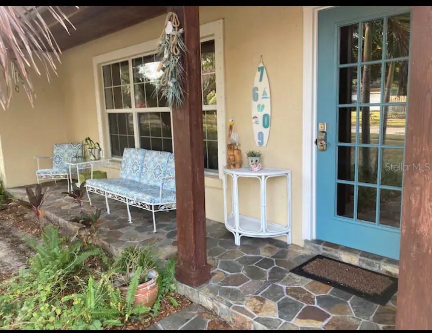 A covered front porch features a stone floor, blue door, and white patio furniture — 7609 SENRAB DRIVE, BRADENTON, FL