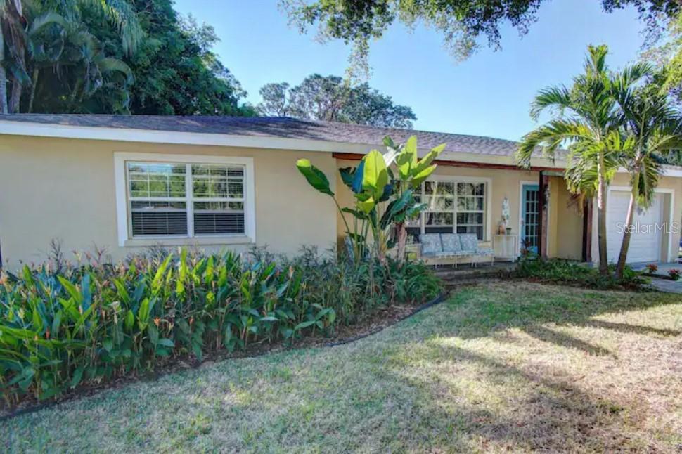 A single-story house with a beige exterior, a front lawn, and tropical landscaping — 7609 SENRAB DRIVE, BRADENTON, FL