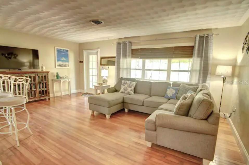 A living room features a sectional sofa, hardwood floors, a television, and a large window — 7609 SENRAB DRIVE, BRADENTON, FL