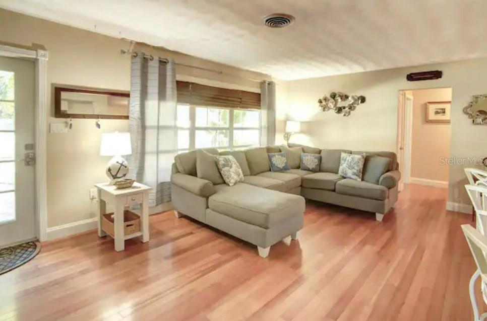 A living room features a large sectional sofa, hardwood floors, and a window with curtains — 7609 SENRAB DRIVE, BRADENTON, FL