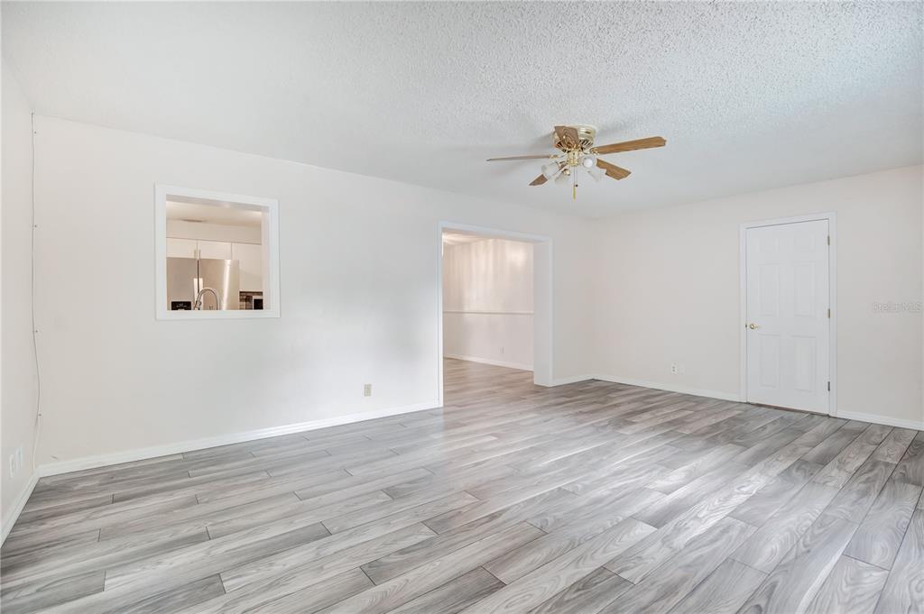 A living room with light gray wood-look flooring, white walls, a ceiling fan, and a pass-through — 605 BOARS HEAD DRIVE, PORT ORANGE, FL