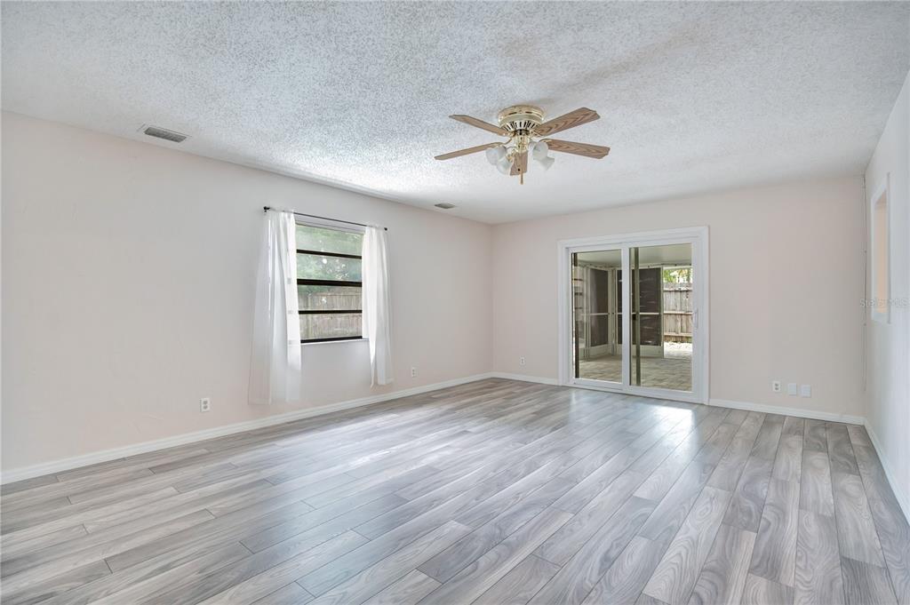 A living room with light-colored walls, wood-look flooring, a ceiling fan, and sliding glass doors — 605 BOARS HEAD DRIVE, PORT ORANGE, FL