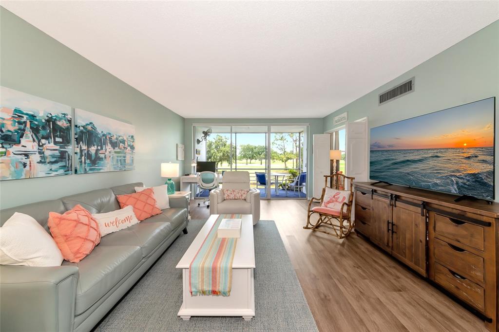 A living room features a gray sofa, a wooden media console, and a screened-in balcony — 7461 W COUNTRY CLUB DRIVE N UNIT 203, SARASOTA, FL
