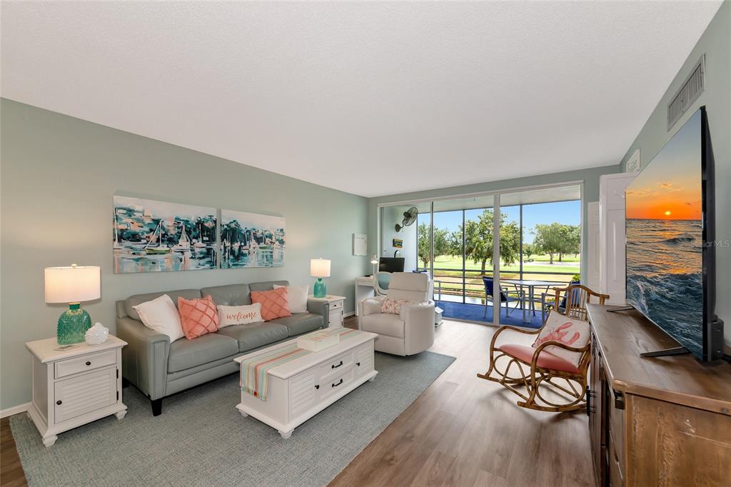 A living room features a gray sofa, white coffee table, rocking chair, and a balcony view — 7461 W COUNTRY CLUB DRIVE N UNIT 203, SARASOTA, FL