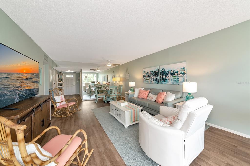 A living room with light green walls, wood flooring, a grey sofa, and a television — 7461 W COUNTRY CLUB DRIVE N UNIT 203, SARASOTA, FL