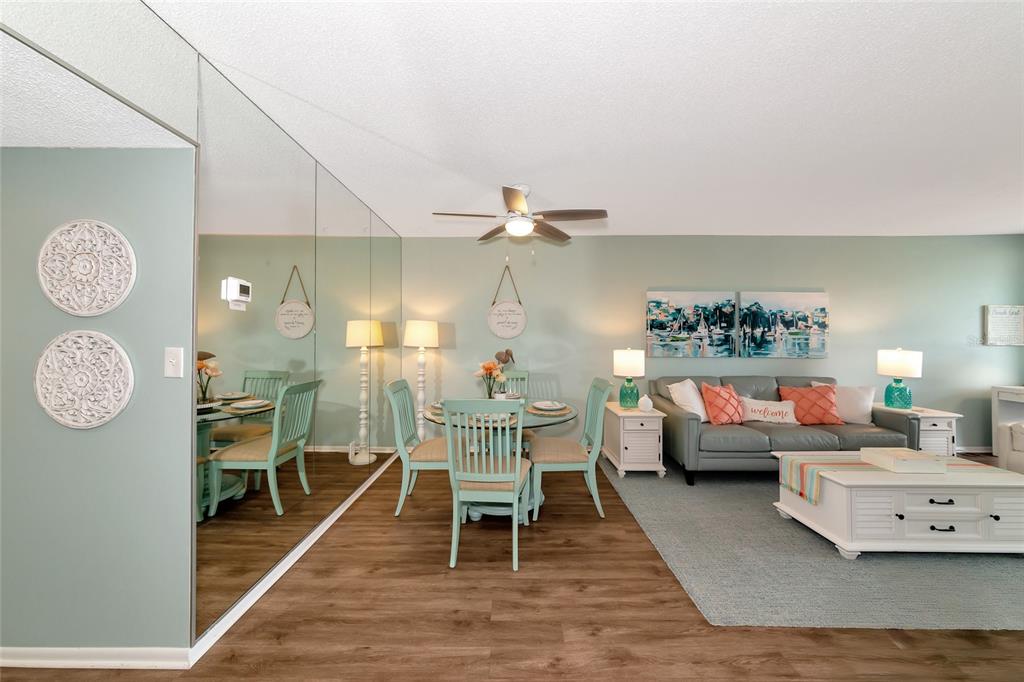 A living and dining area features light blue walls, wood-look flooring, and a mirrored wall — 7461 W COUNTRY CLUB DRIVE N UNIT 203, SARASOTA, FL
