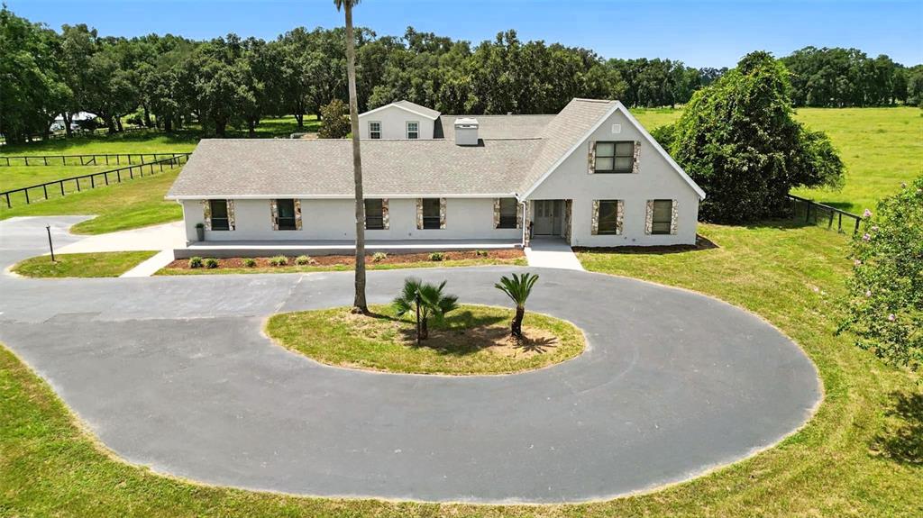 An aerial view of a light-colored house with a circular driveway and surrounding grassy fields — 1960 SE 150TH STREET, SUMMERFIELD, FL