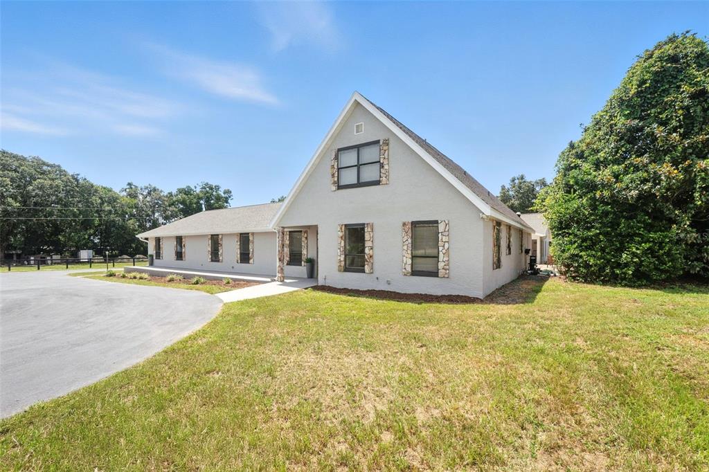 A light-colored house with stone accents and a large gable roof sits on a lawn — 1960 SE 150TH STREET, SUMMERFIELD, FL