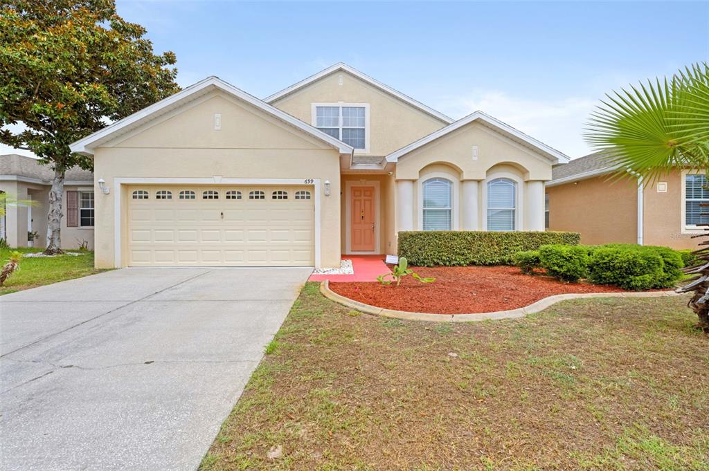 A single-story suburban house with a beige stucco exterior, a two-car garage, and landscaping — 699 WINTHROP DRIVE, SPRING HILL, FL