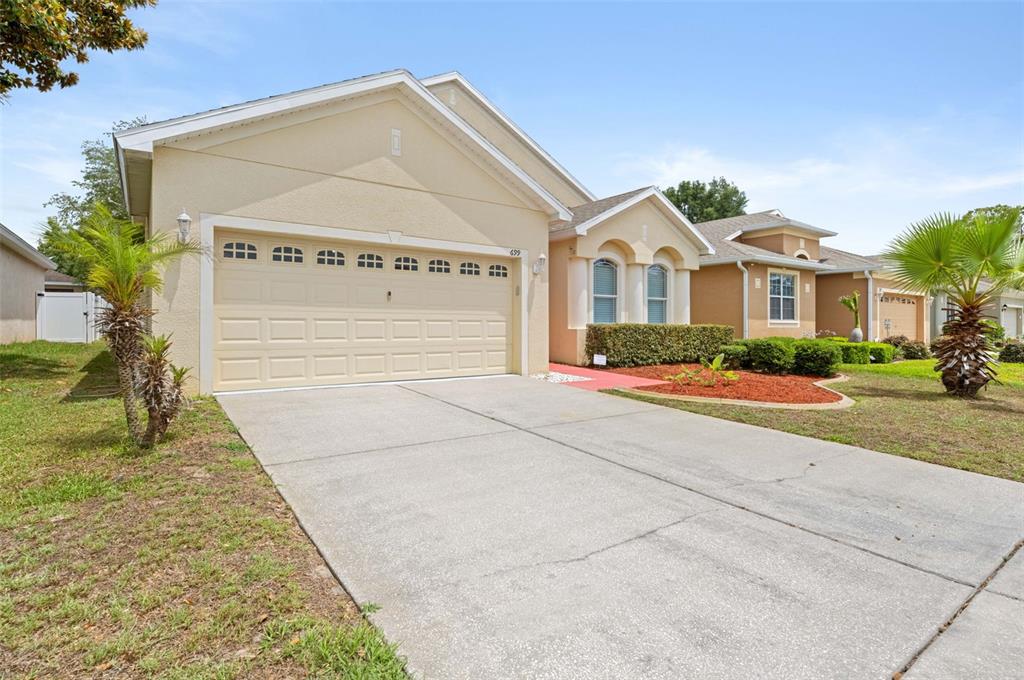 A single-story suburban house with a beige stucco exterior, a two-car garage, and a driveway — 699 WINTHROP DRIVE, SPRING HILL, FL