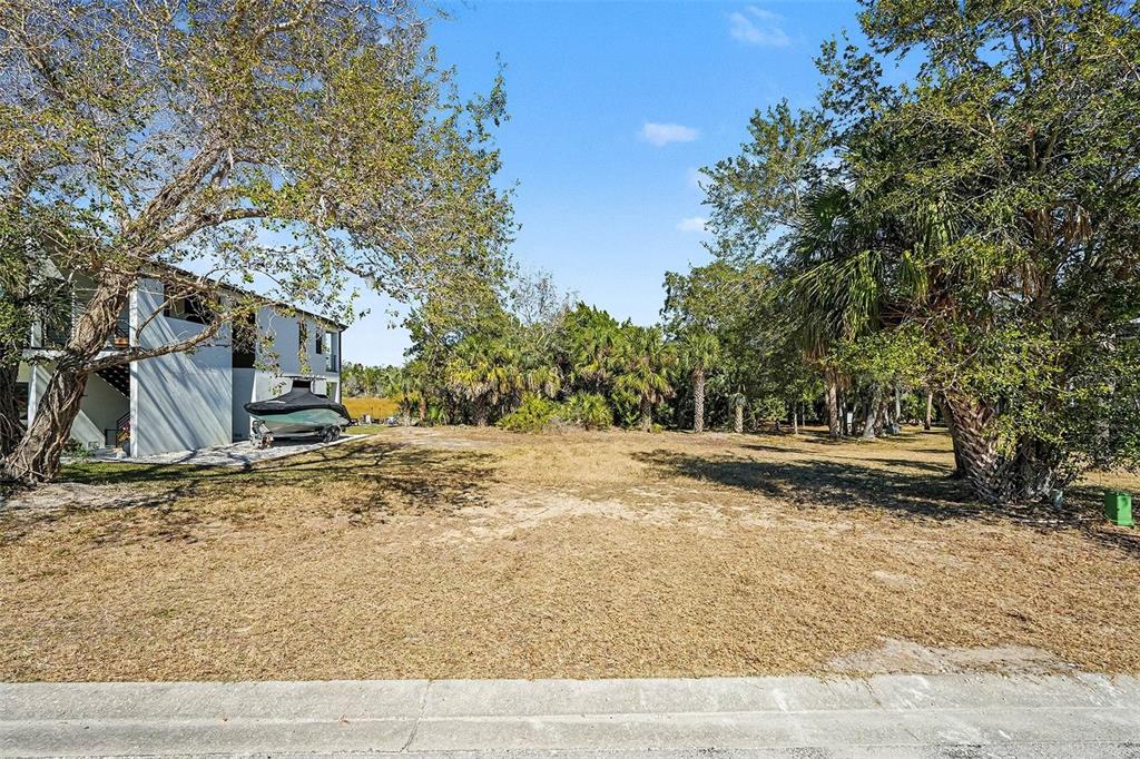 A vacant, grassy lot sits next to a multi-story house with a boat parked underneath — 7657 GULF WAY, HUDSON, FL