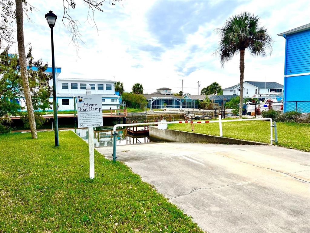 A concrete boat ramp leads into a canal between residential buildings under a cloudy sky — 7657 GULF WAY, HUDSON, FL