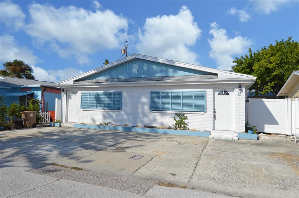A single-story duplex with white brick walls, blue shutters, and a concrete driveway — 156 146TH AVENUE E UNIT A, MADEIRA BEACH, FL
