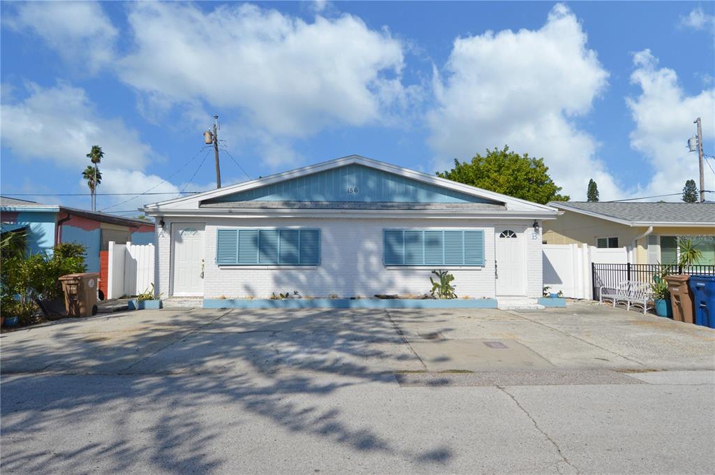 A single-story duplex with white brick walls, blue shutters, and a concrete driveway — 156 146TH AVENUE E UNIT A, MADEIRA BEACH, FL