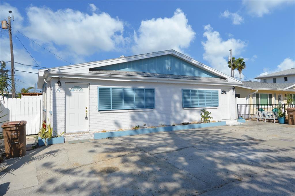 A single-story duplex with white brick walls, blue shutters, and a concrete driveway — 156 146TH AVENUE E UNIT A, MADEIRA BEACH, FL