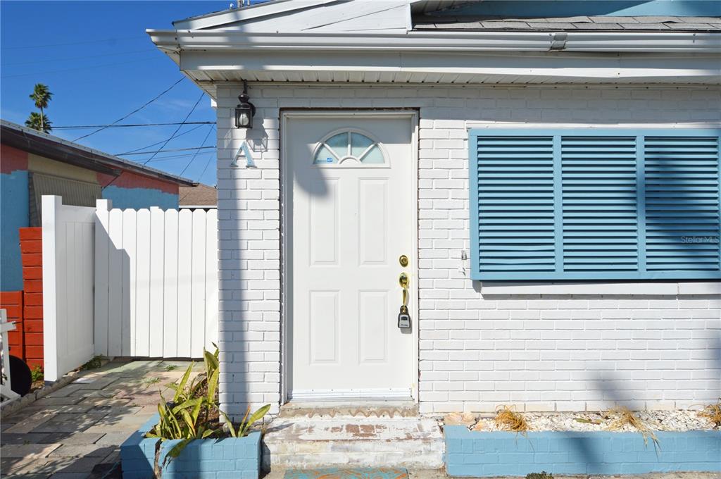A white brick exterior features a front door with a lockbox and blue shutters — 156 146TH AVENUE E UNIT A, MADEIRA BEACH, FL
