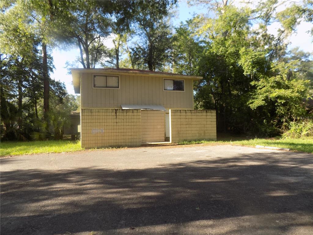 A two-story building with tan vertical siding and a lower-level concrete block privacy wall — 713 SW 69 STREET, GAINESVILLE, FL
