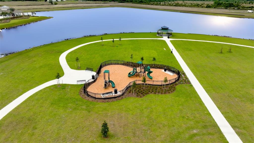 An aerial view shows a fenced playground with equipment situated on a grassy lawn near a lake — 3781 MALAWI TRAIL, ST CLOUD, FL