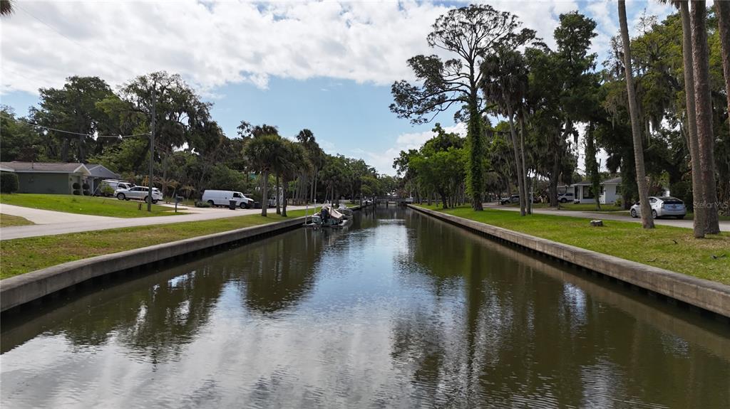 A narrow canal runs between grassy banks lined with palm trees and residential houses — 96 E BAYSHORE DRIVE, PORT ORANGE, FL