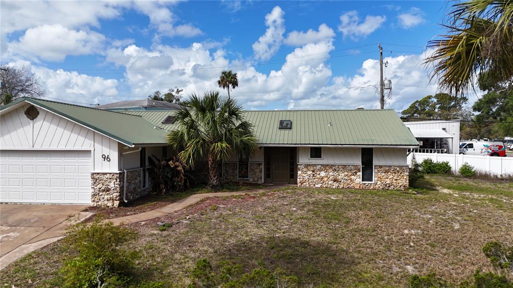 A single-story house with a green metal roof, stone facade, and a white garage — 96 E BAYSHORE DRIVE, PORT ORANGE, FL