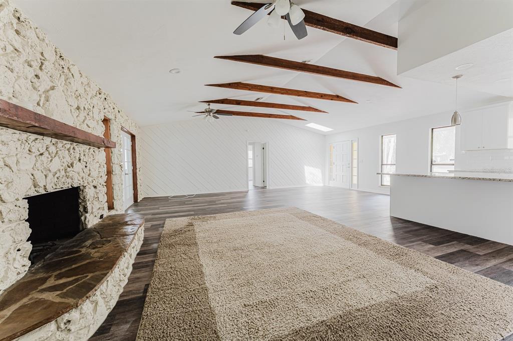 A living room features a stone fireplace, wood-look flooring, exposed ceiling beams, and white walls — 96 E BAYSHORE DRIVE, PORT ORANGE, FL