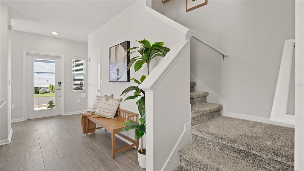 An entryway features a wooden bench, a potted plant, and a carpeted staircase — 6083 WELLBEING WAY, CLERMONT, FL
