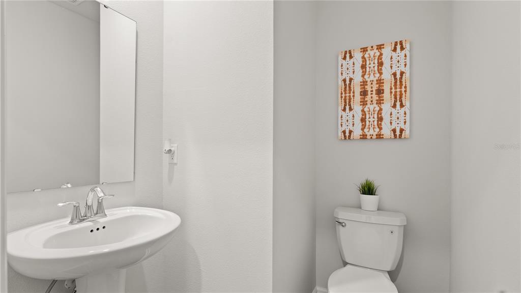 A half bathroom features a white pedestal sink, a toilet, and a decorative wall canvas — 6083 WELLBEING WAY, CLERMONT, FL