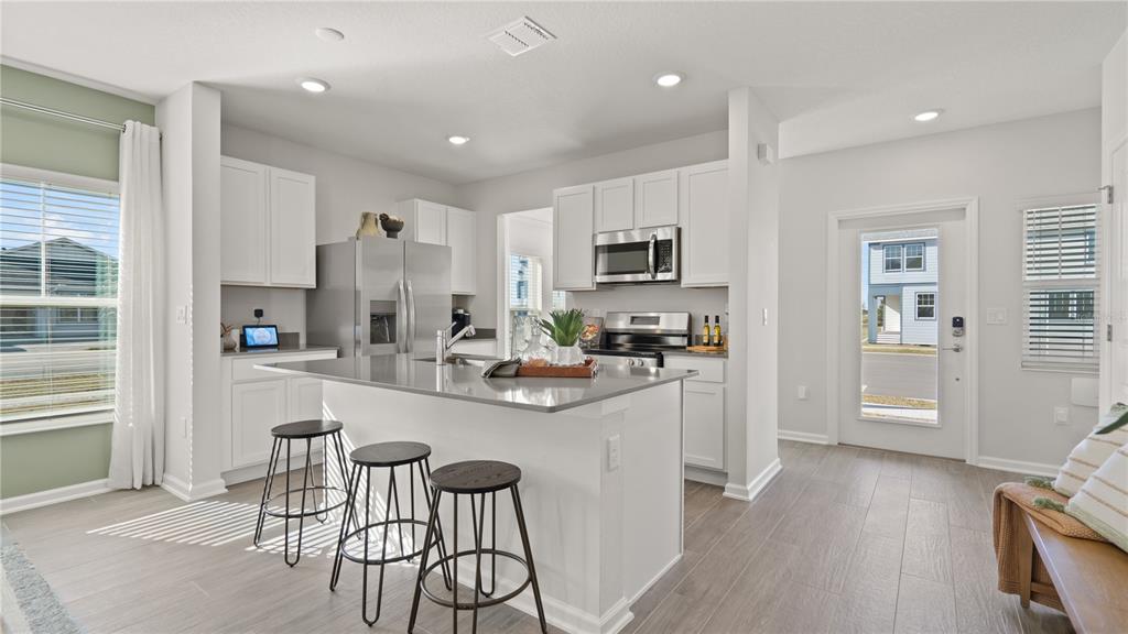 A modern kitchen features white cabinets, a gray island with bar stools, and stainless appliances — 6083 WELLBEING WAY, CLERMONT, FL