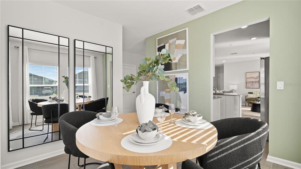 A dining area features a round wooden table, black chairs, wall mirrors, and sage green walls — 6083 WELLBEING WAY, CLERMONT, FL