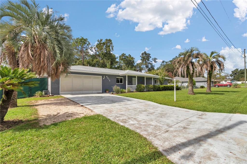 A single-story gray brick house features a concrete driveway, palm trees, and a large lawn — 6072 E RUSH STREET, INVERNESS, FL