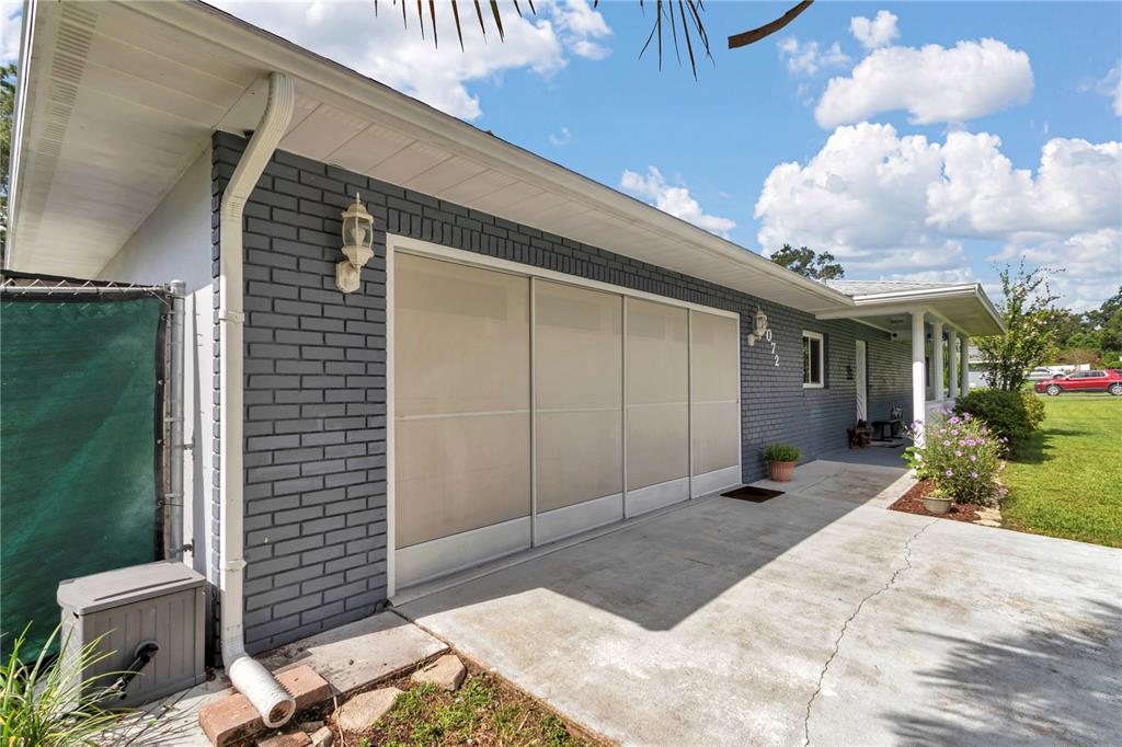 A gray brick house exterior features a sliding screen door over the garage opening — 6072 E RUSH STREET, INVERNESS, FL