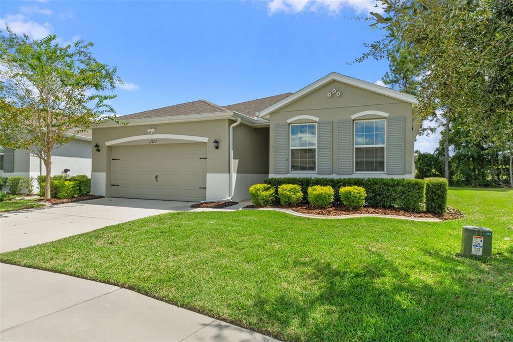 A single-story suburban house with a two-car garage, beige stucco exterior, and a front lawn — 17807 GARSALASO CIRCLE, BROOKSVILLE, FL