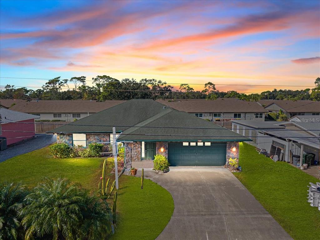 A single-story house with a stone facade, green roof, and a two-car garage at sunset — 1560 INGRAM AVENUE, SARASOTA, FL