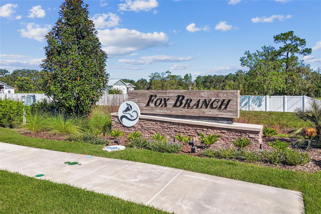 A stone monument sign for Fox Branch stands beside a sidewalk under a blue sky — 4518 LAKE FOX DRIVE, LAKELAND, FL