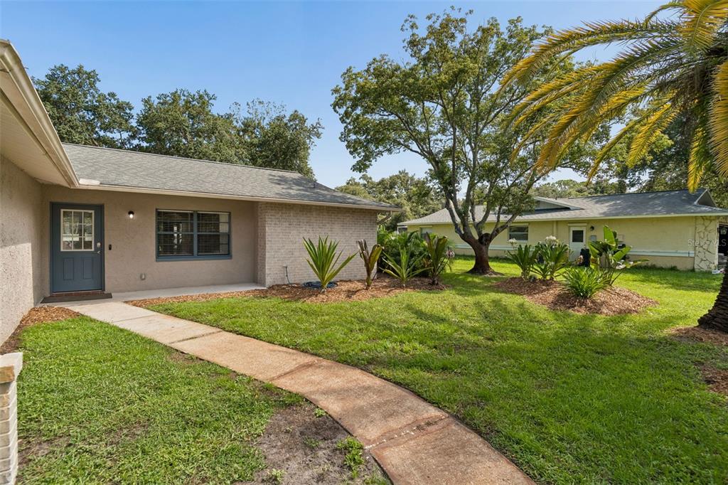 A beige house with a gray roof and a curved concrete walkway leading to the entrance — 9329 AMAZON DRIVE, NEW PORT RICHEY, FL