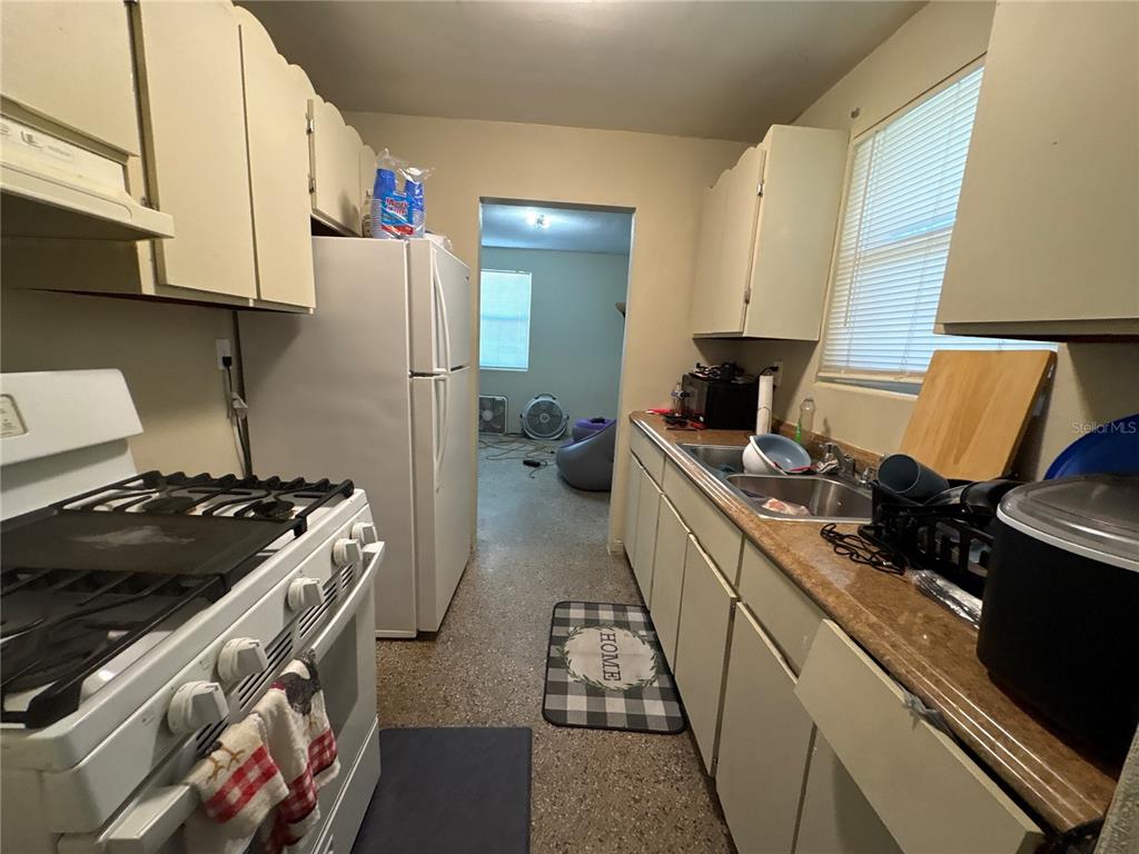 A galley kitchen features white cabinets, a gas stove, a refrigerator, and a stainless sink — 532 S CAROLINE STREET, DAYTONA BEACH, FL