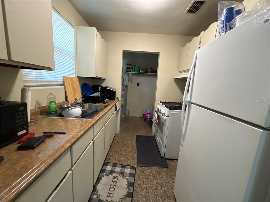 A galley kitchen features white cabinets, a laminate countertop, a sink, and white appliances — 532 S CAROLINE STREET, DAYTONA BEACH, FL