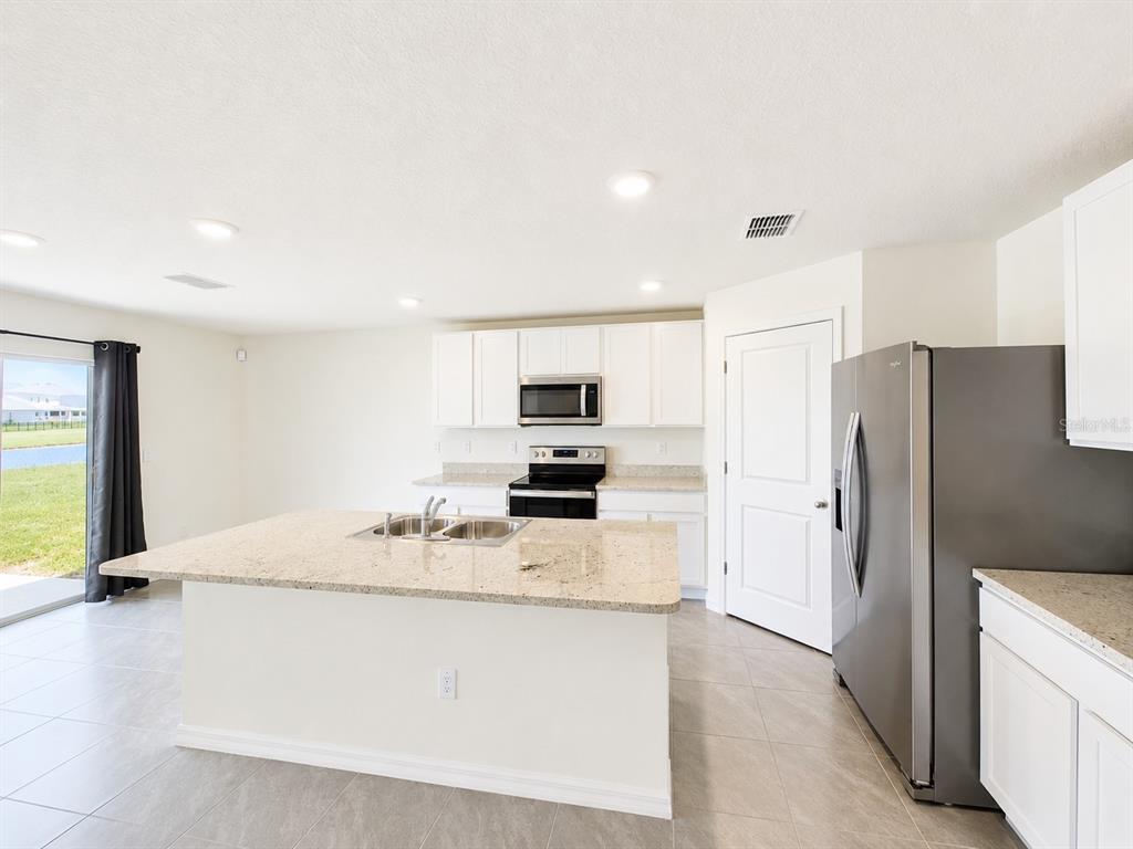 A kitchen features white cabinets, granite countertops, a center island, and stainless steel appliances — 10642 CHIPPEWA DRIVE, PARRISH, FL