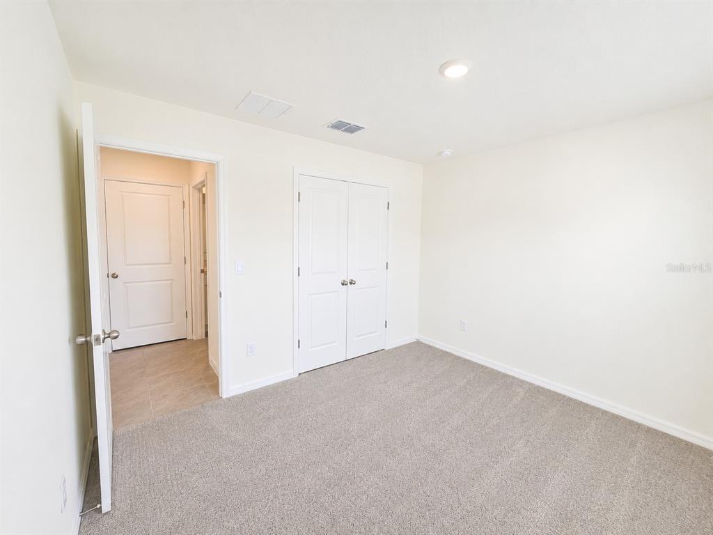 A bedroom with beige carpet, white walls, a closet, and an open doorway to a bathroom — 10642 CHIPPEWA DRIVE, PARRISH, FL