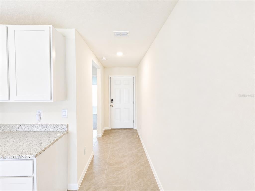 A hallway with tile flooring leads to a white front door next to kitchen cabinets — 10642 CHIPPEWA DRIVE, PARRISH, FL