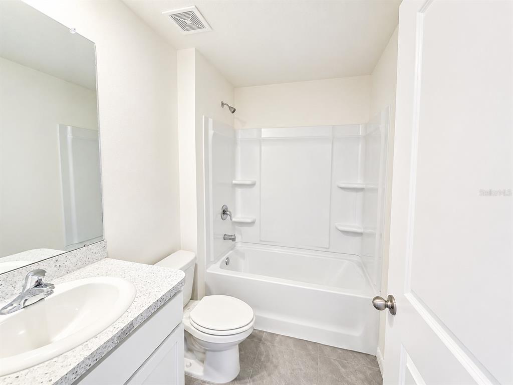 A bathroom features a white vanity, a toilet, and a shower-tub combination with white walls — 10642 CHIPPEWA DRIVE, PARRISH, FL