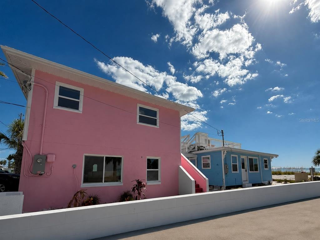 A pink two-story house stands next to a smaller blue house under a sunny sky — 12609 SUNSHINE LANE, TREASURE ISLAND, FL