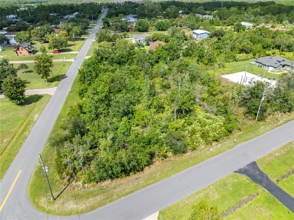 An aerial view shows a vacant, tree-covered corner lot situated between two paved roads — 2240 BRONCO DR, ST CLOUD, FL