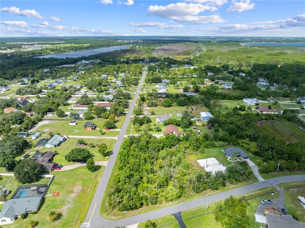 An aerial view shows a residential neighborhood with houses, wooded lots, and a nearby lake — 2240 BRONCO DR, ST CLOUD, FL