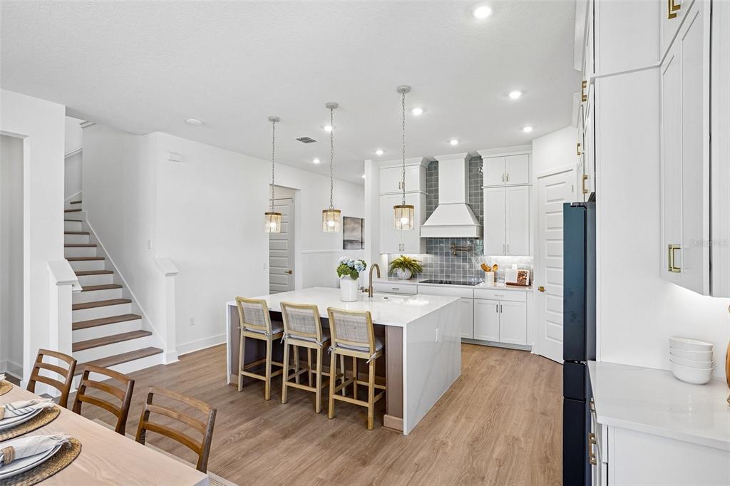 A modern kitchen features white cabinetry, a central island with bar seating, and wood flooring — 17428 HONEYBELL TANGELO COURT, WINTER GARDEN, FL