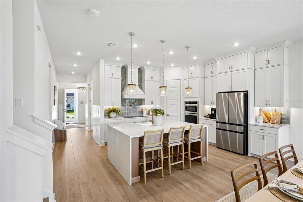 A bright kitchen features white cabinetry, a large central island with seating, and wood flooring — 17428 HONEYBELL TANGELO COURT, WINTER GARDEN, FL