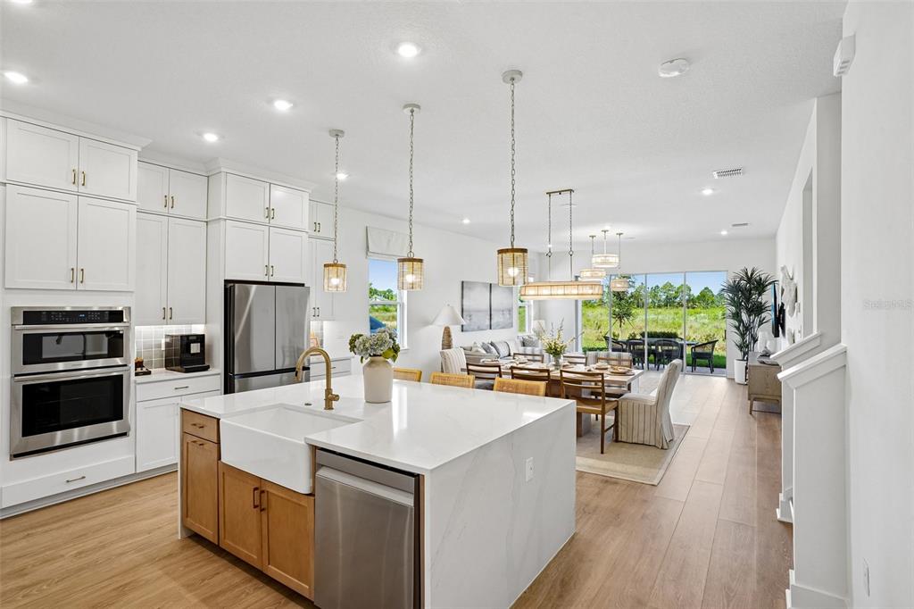 A modern kitchen with white cabinets, a wood-toned island, and an open-concept dining area beyond — 17428 HONEYBELL TANGELO COURT, WINTER GARDEN, FL