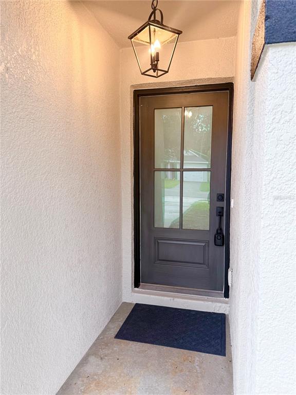A dark-framed glass-paneled front door is set within a stucco entryway with a hanging lantern — 1112 W 7TH STREET, SANFORD, FL